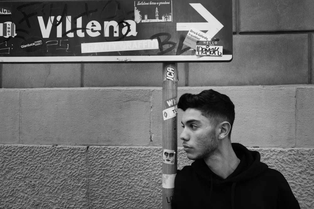 A young man stands beneath a directional street sign