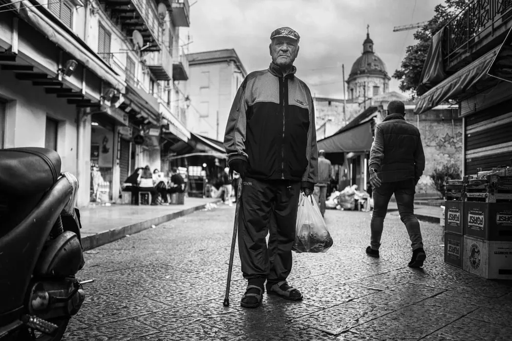 An older man walks through a market using a walking stick