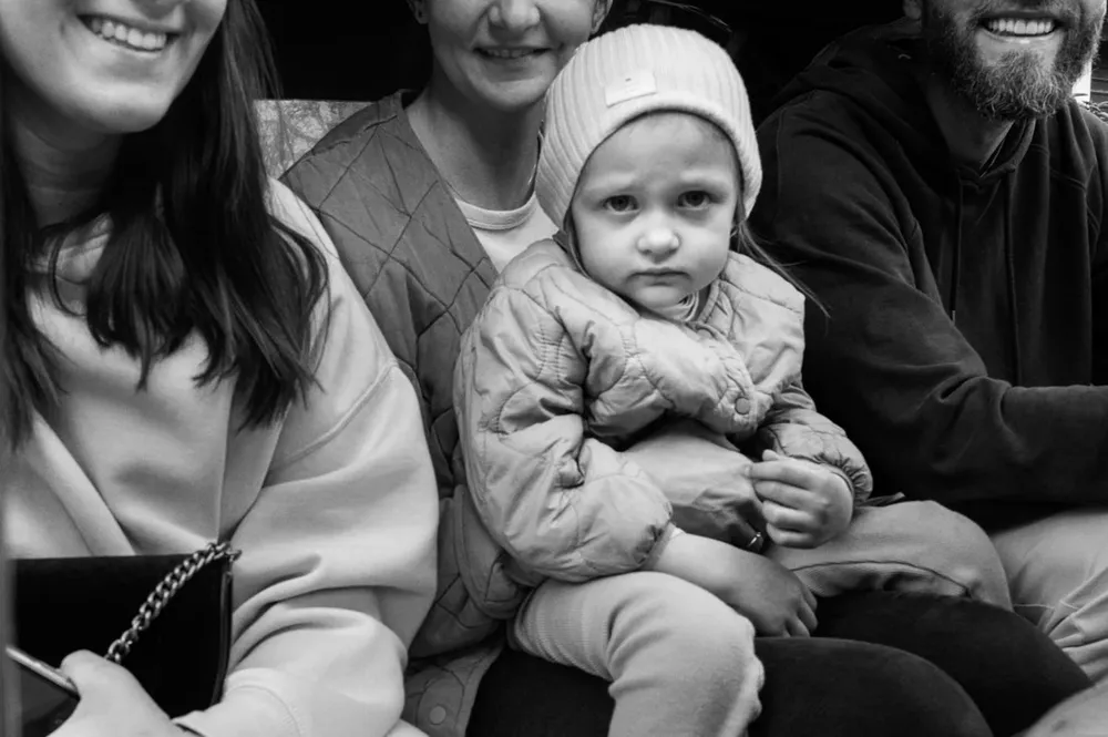 A baby in a knitted hat sits among smiling adults