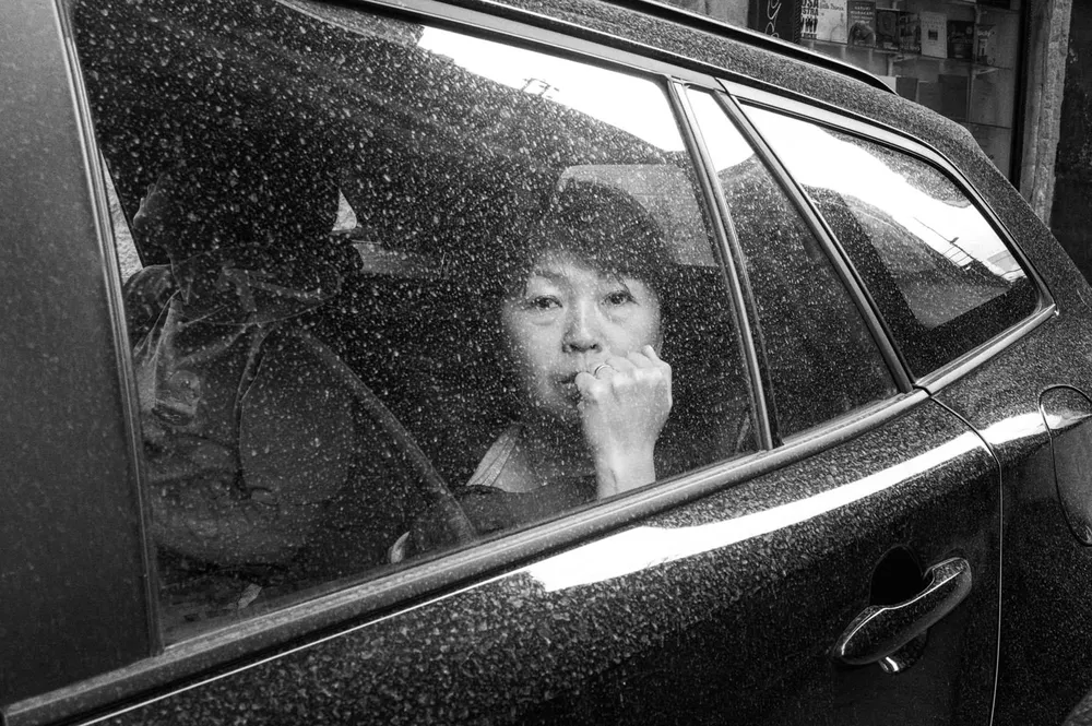 A child looks through a rain-speckled car window