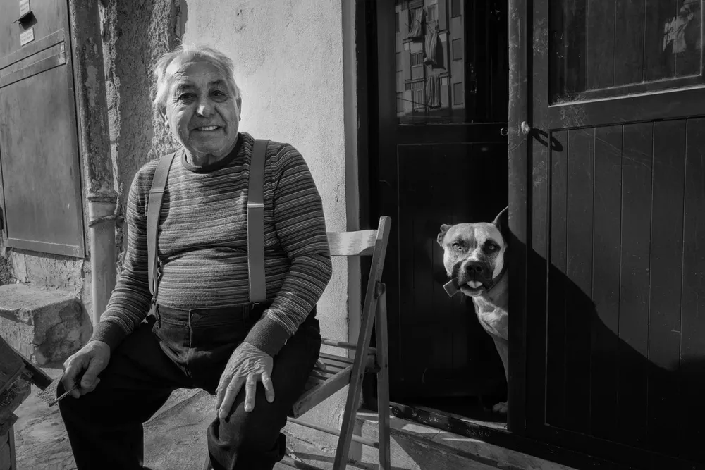 A seated woman smiles beside a dog peeking through a doorway