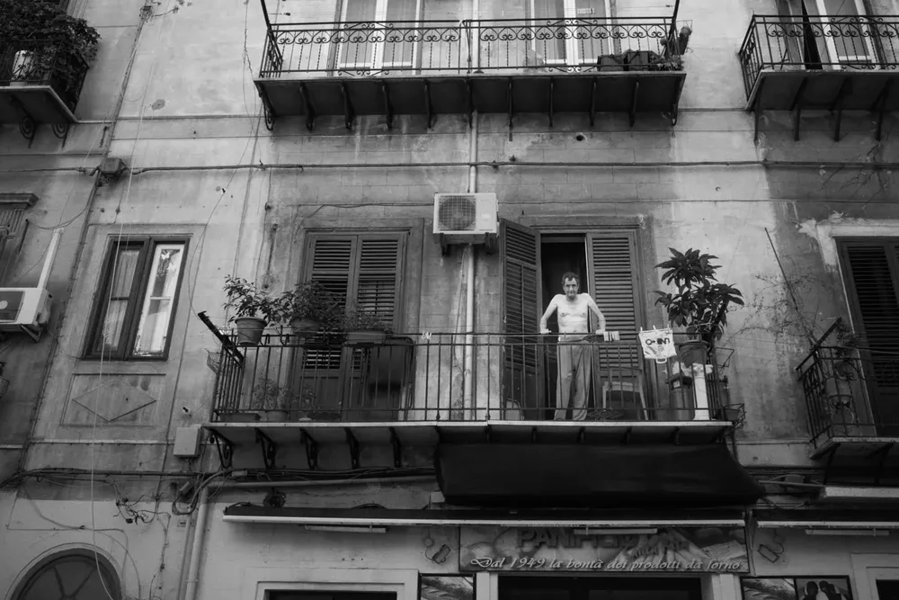 A person stands on a balcony above a narrow street