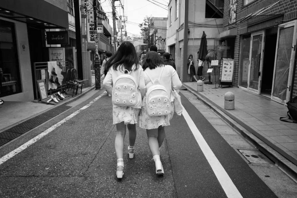 Two women walk arm in arm down a narrow street