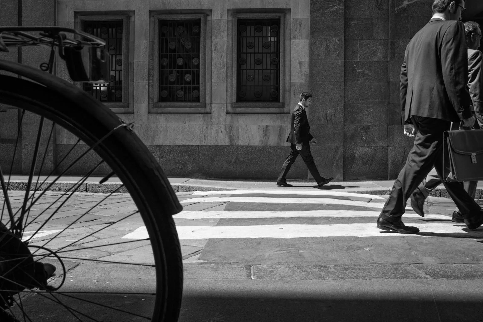 A bicycle wheel frames suited pedestrians crossing a street