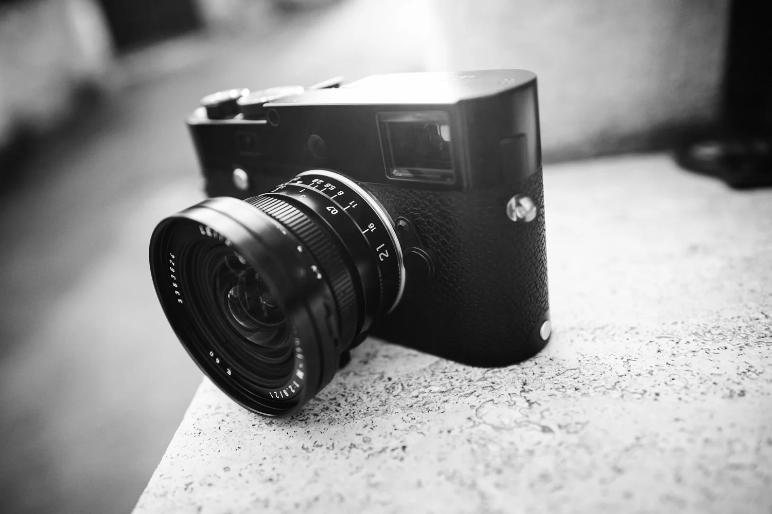A black Leica camera and wide-angle lens rest on a stone surface