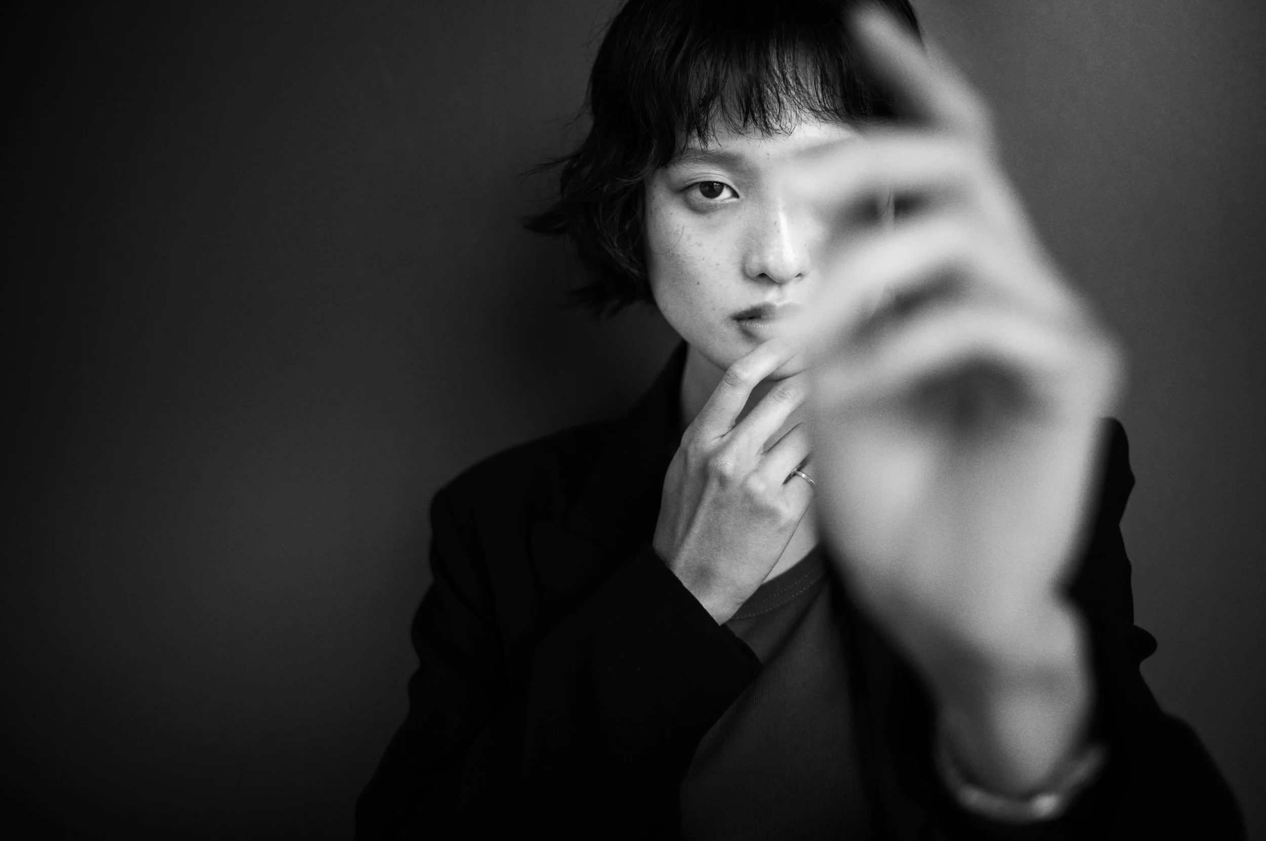 A black and white portrait with a blurred raised hand in the foreground