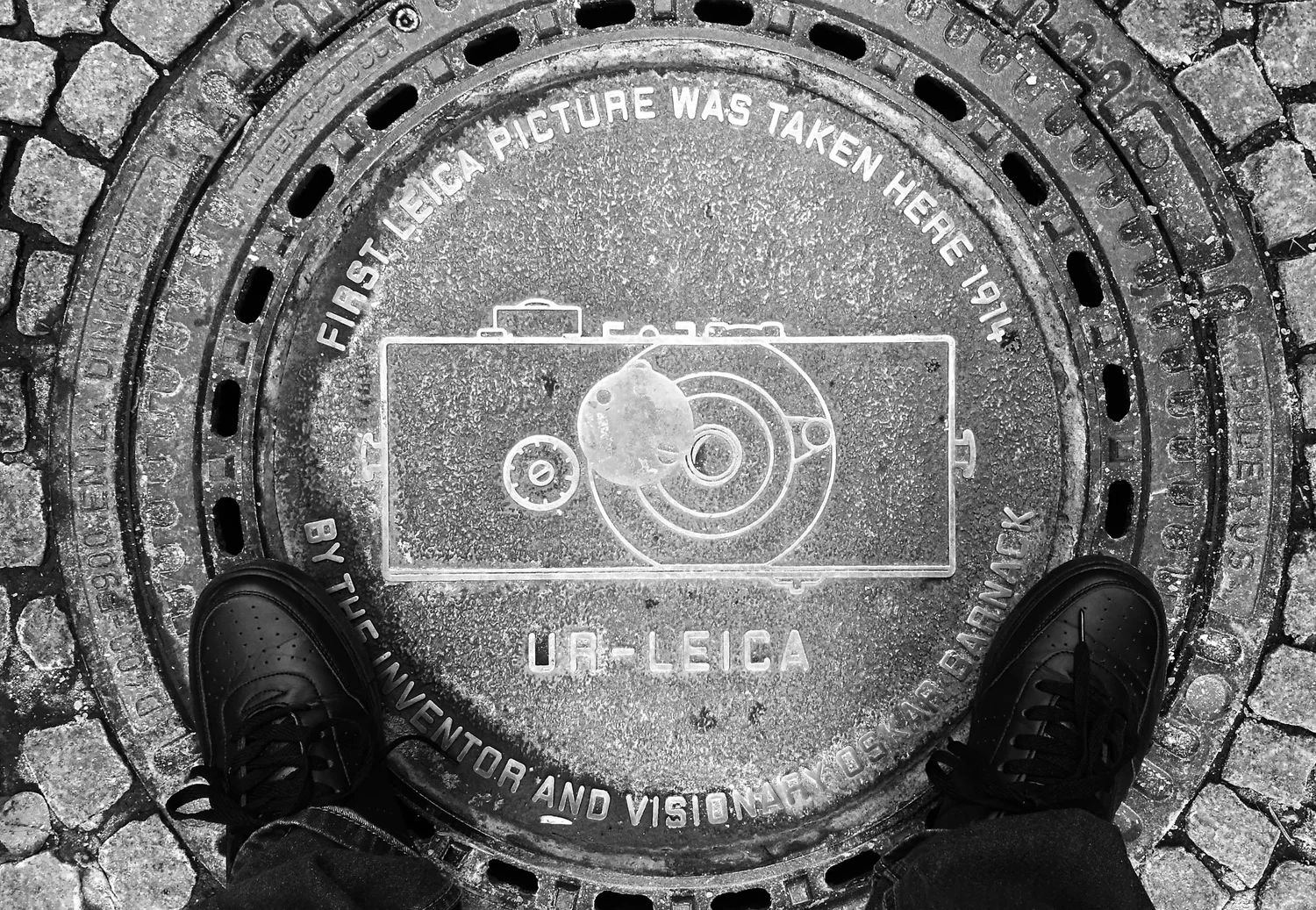 A commemorative Leica manhole cover photographed between the photographer's shoes