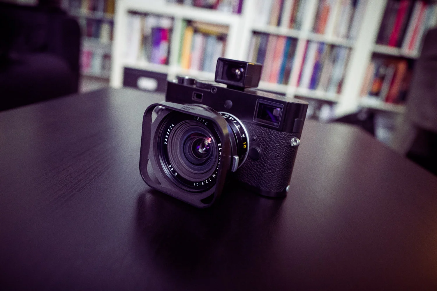 A Leica camera rests on a table in front of bookshelves