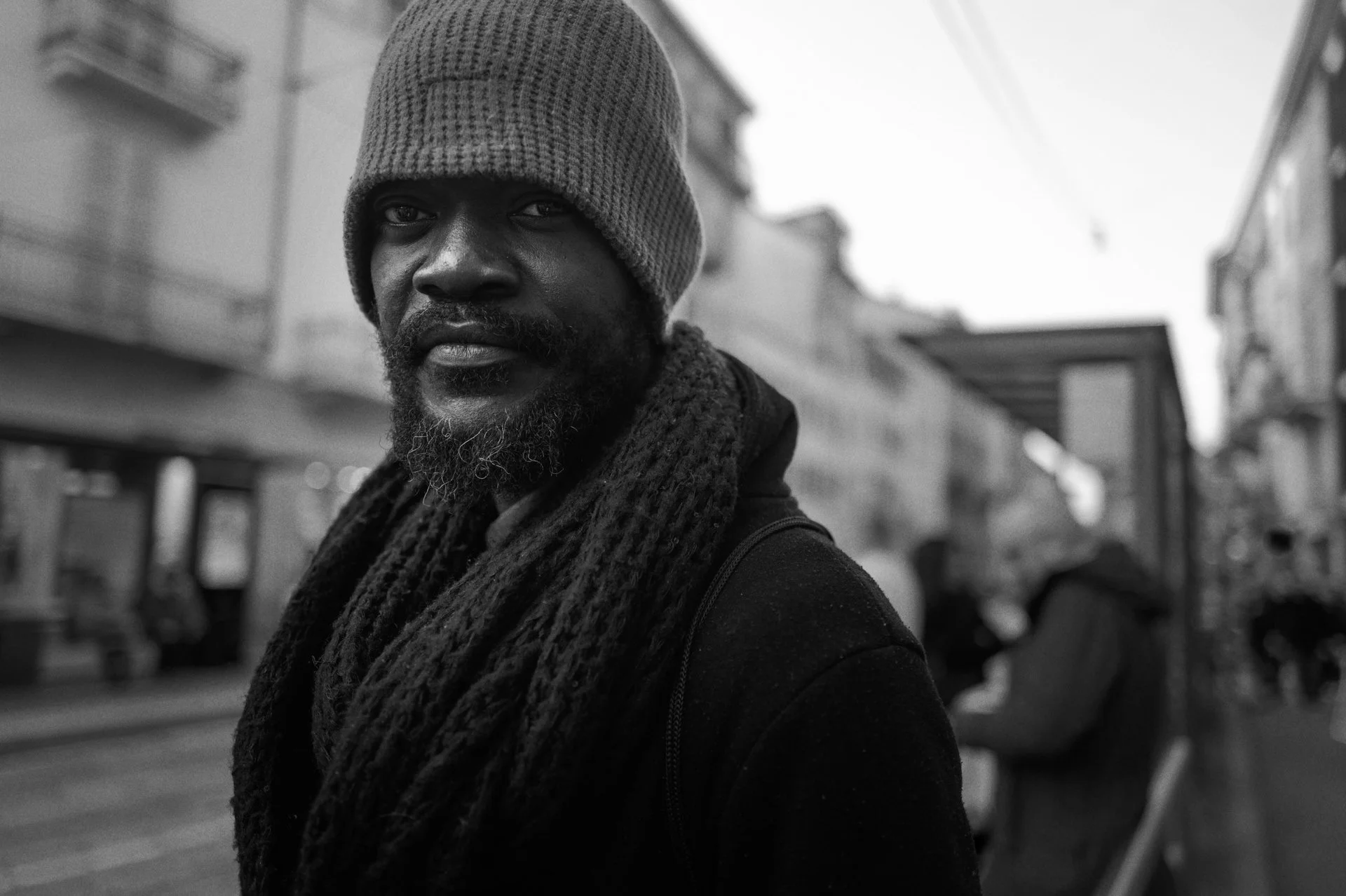 A man in a knitted cap and scarf looks toward the camera