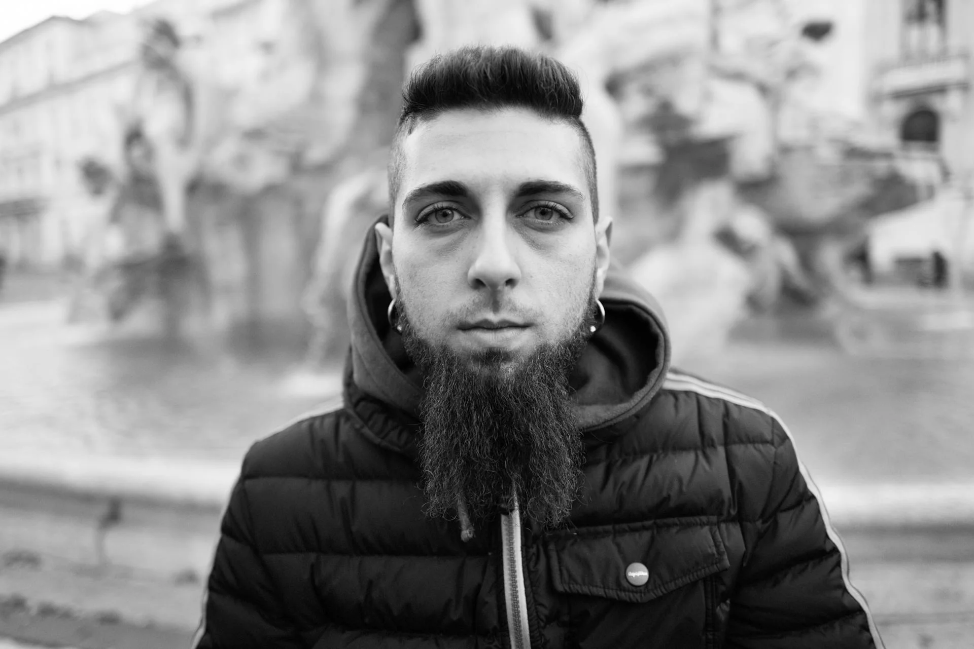 A man with a long pointed beard poses near a fountain