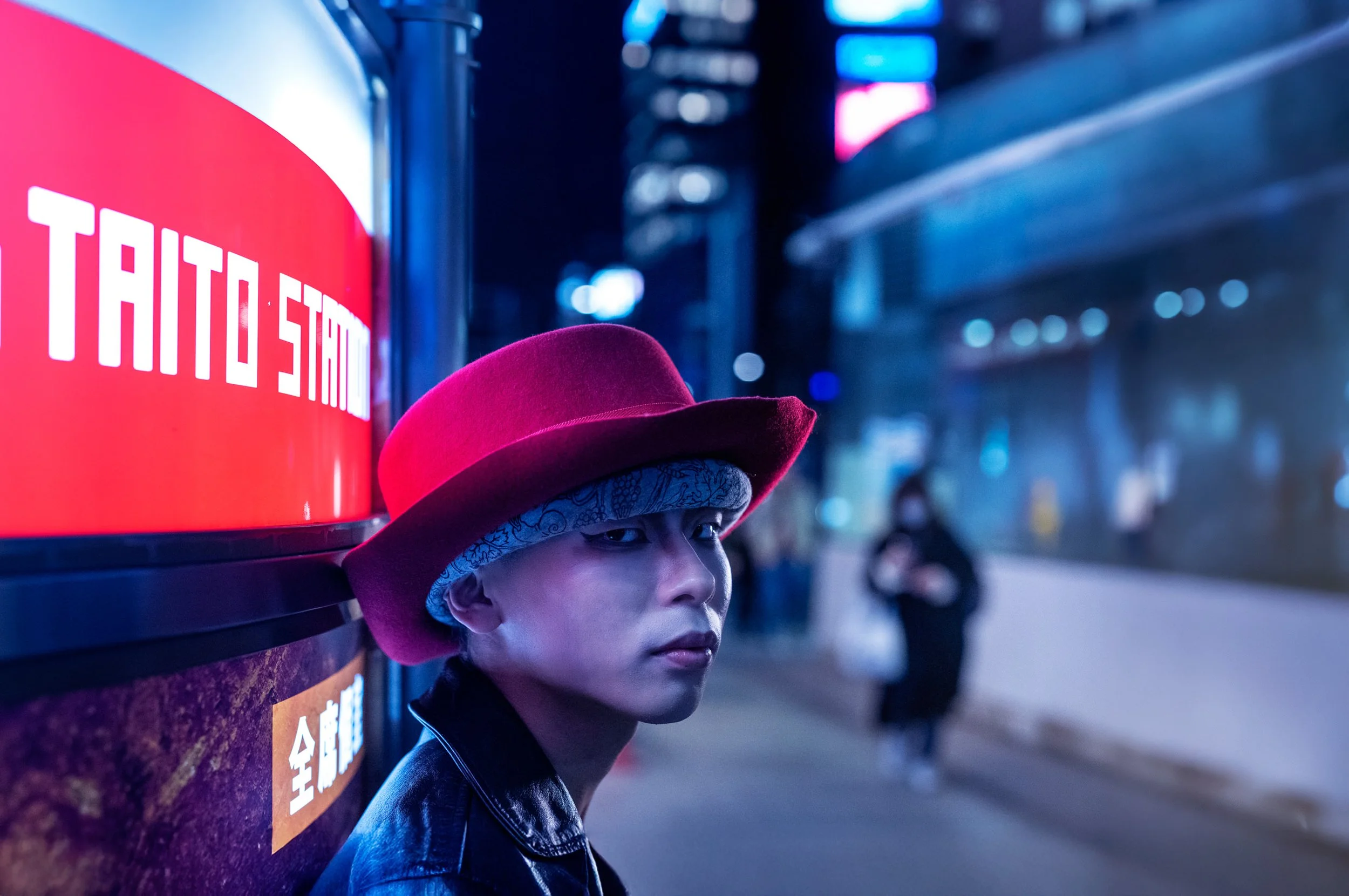 A man in a red hat stands beneath colorful illuminated signs