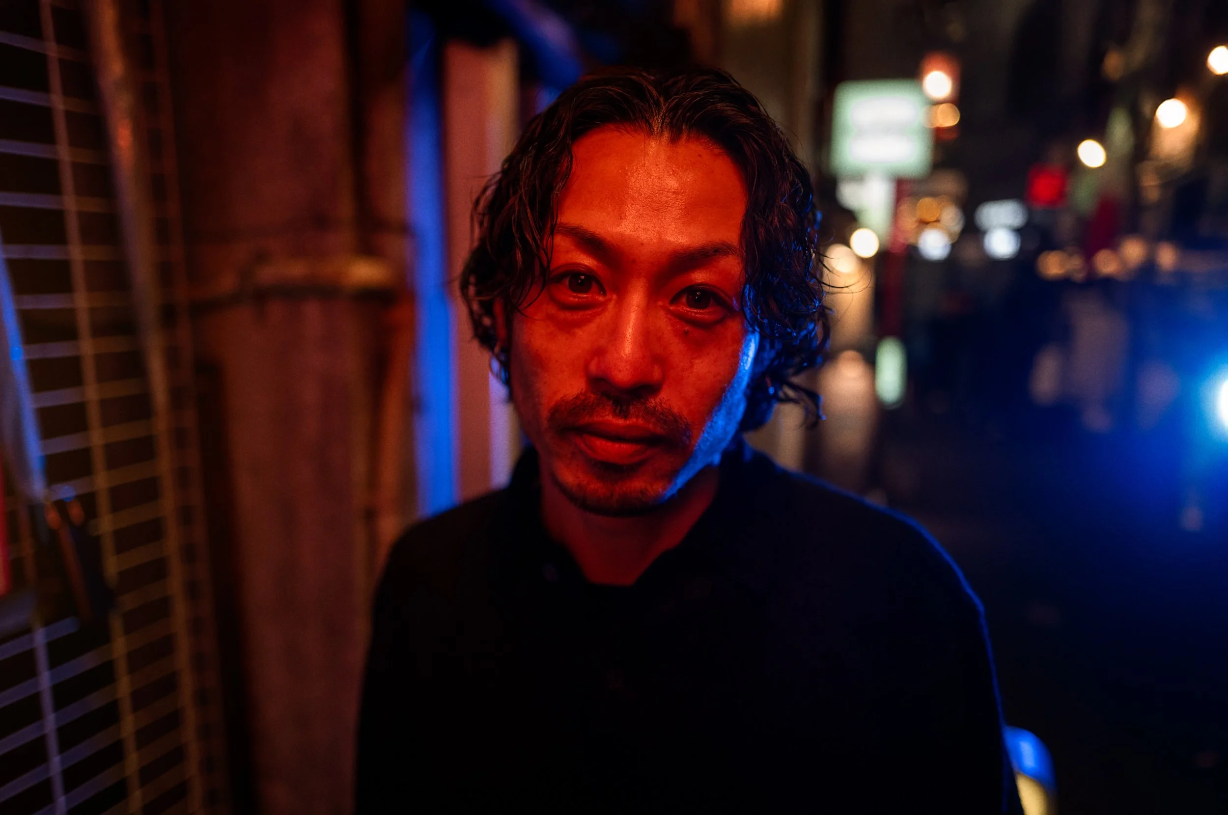 A man stands in a night street lit by red and blue light