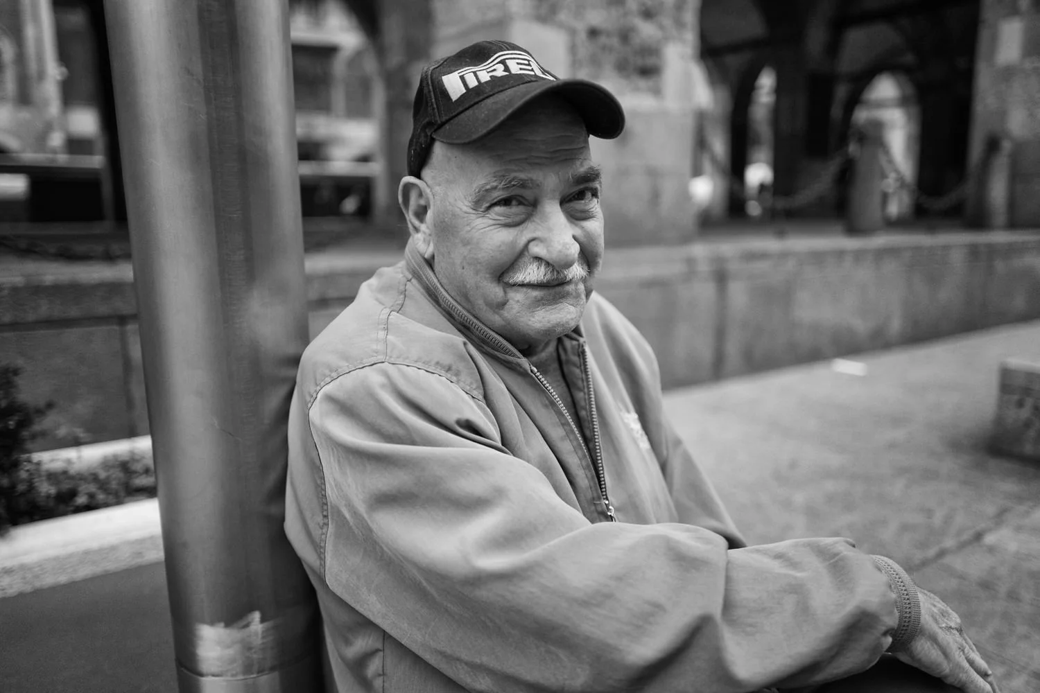 An older man in a cap sits with his arms resting in front of him