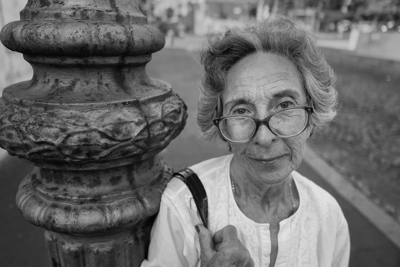 An older woman wearing glasses looks toward the camera