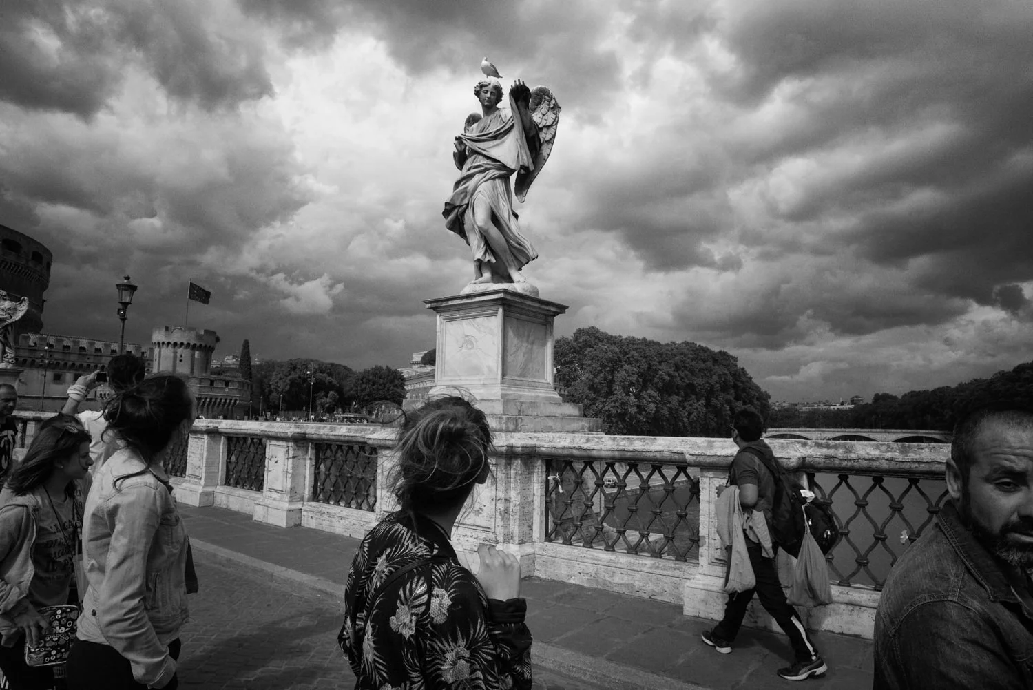 Pedestrians pass an angel statue on a bridge