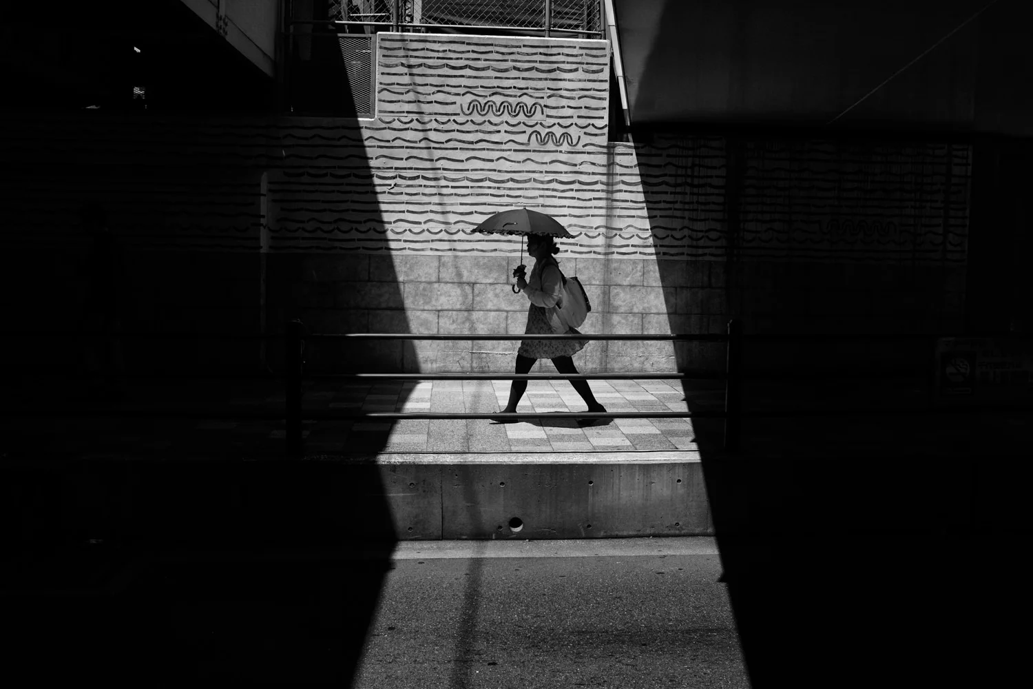 A person carrying an umbrella crosses a bright opening between dark walls