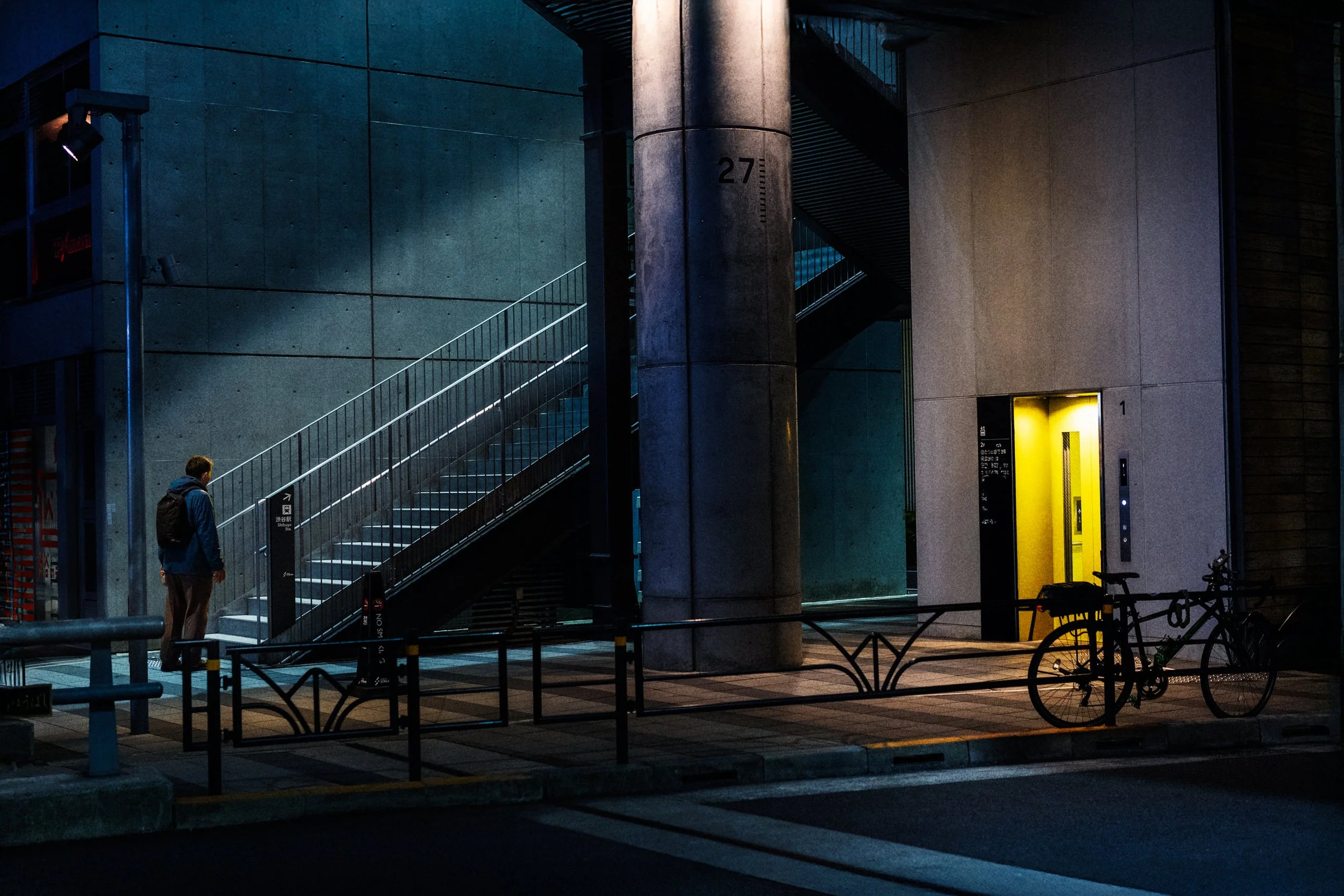 A person walks past a stairway and a brightly lit doorway at night