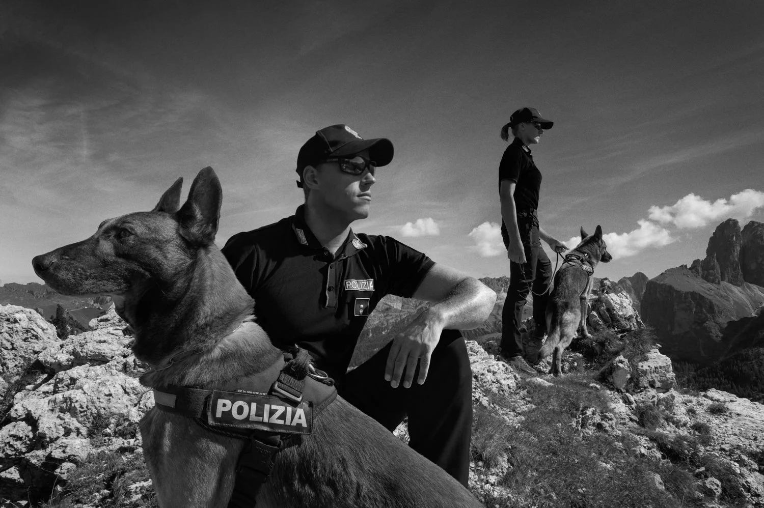 A police officer and working dog rest on rocky mountain terrain