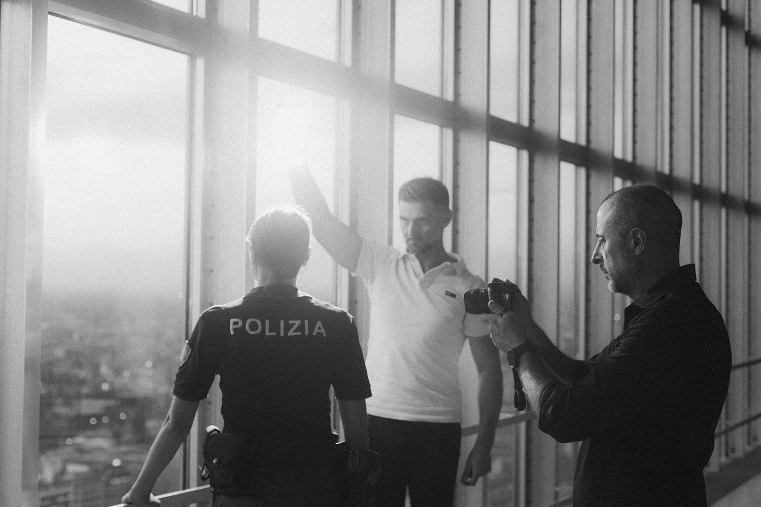 Police officers stand by tall windows in strong sunlight