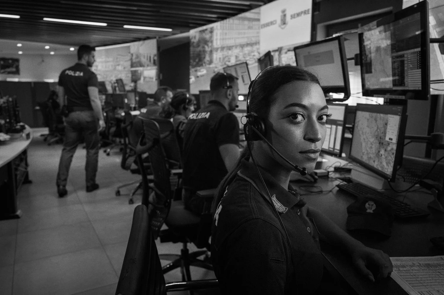 A police operator wearing a headset sits at a workstation