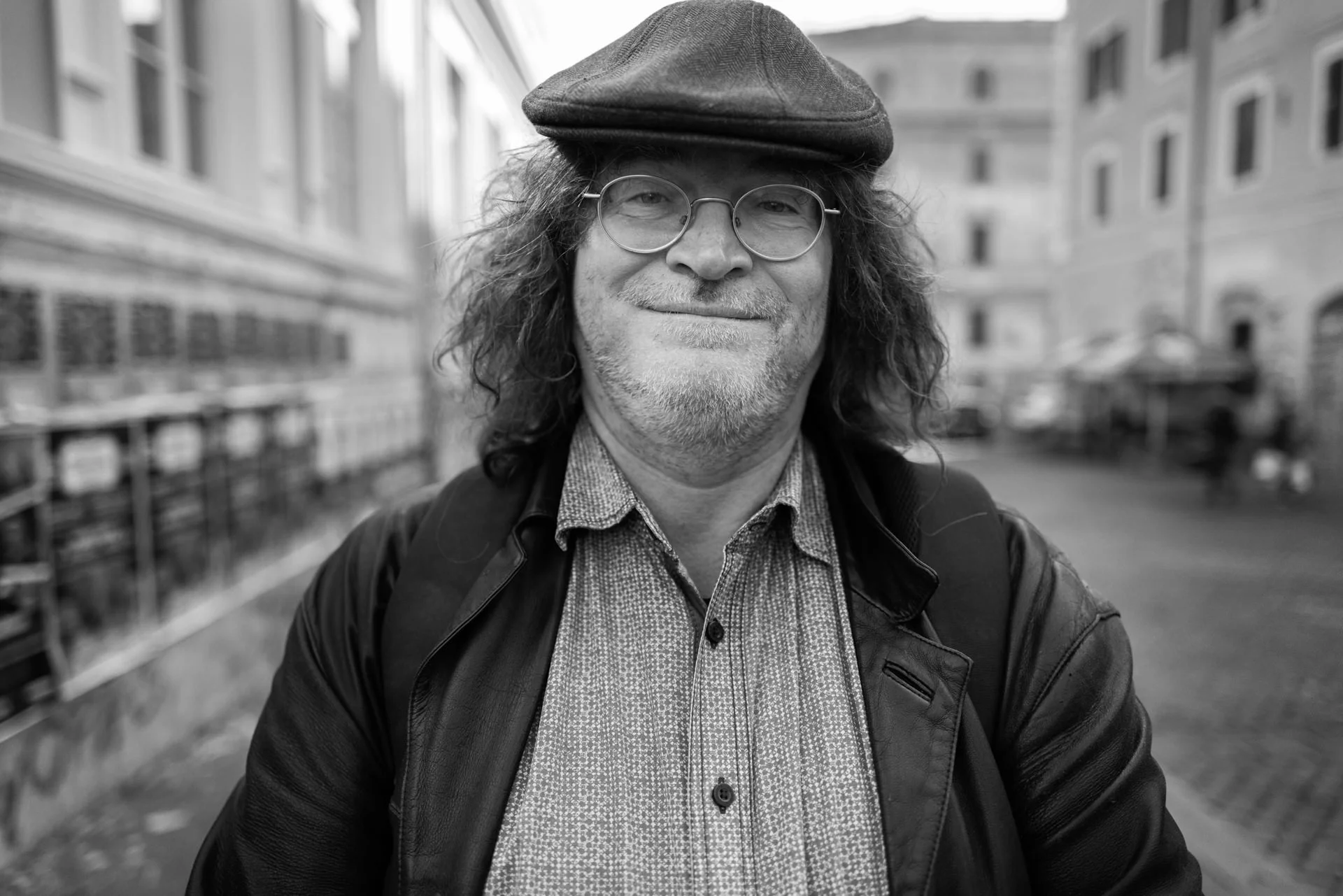 A smiling man in a cap and glasses stands in a square