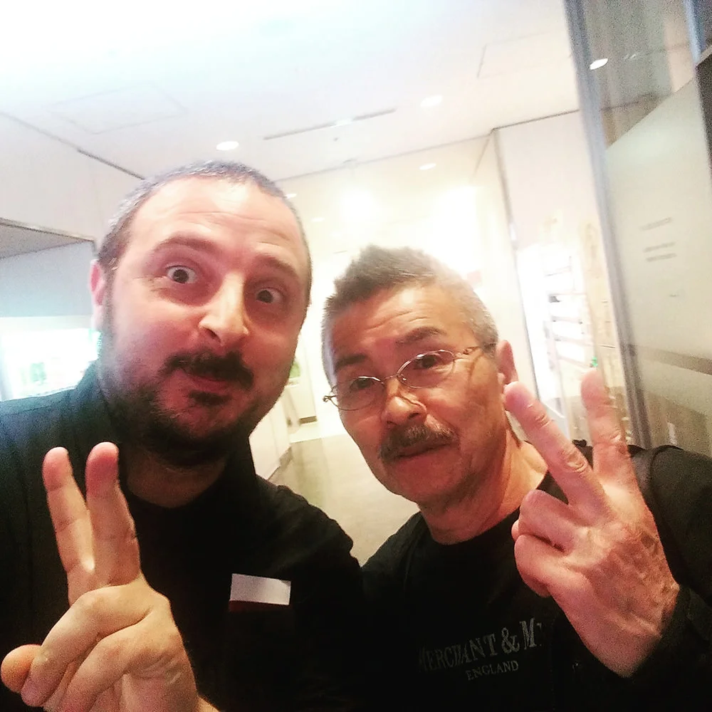 Two men pose together making hand gestures