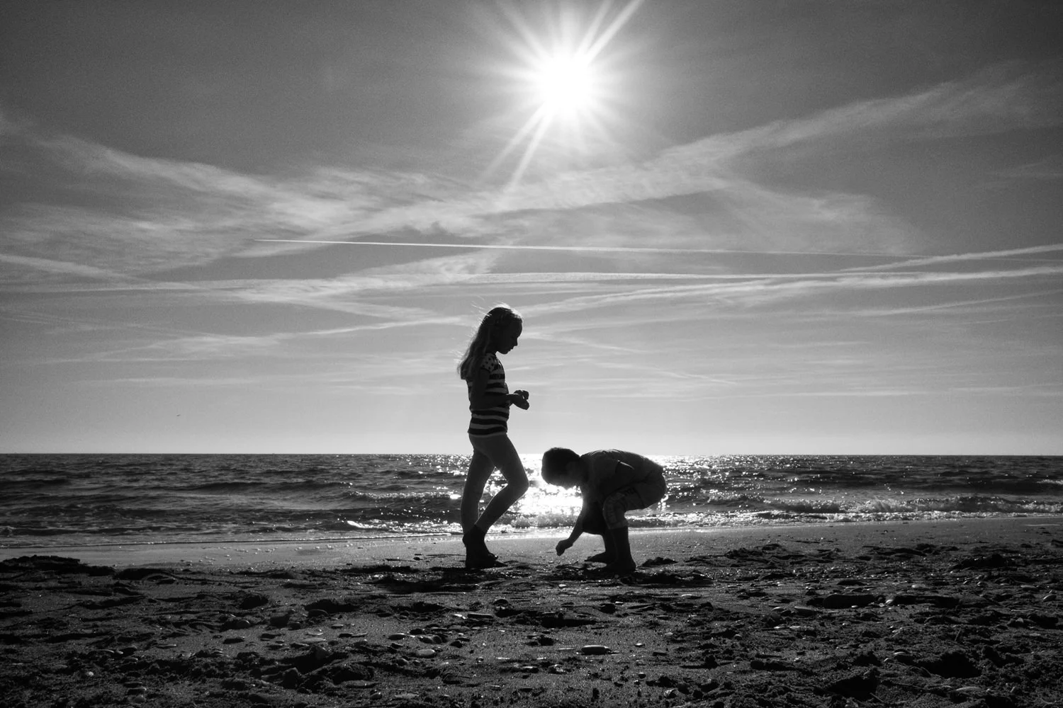 Two silhouetted figures stand on the shoreline beneath the sun