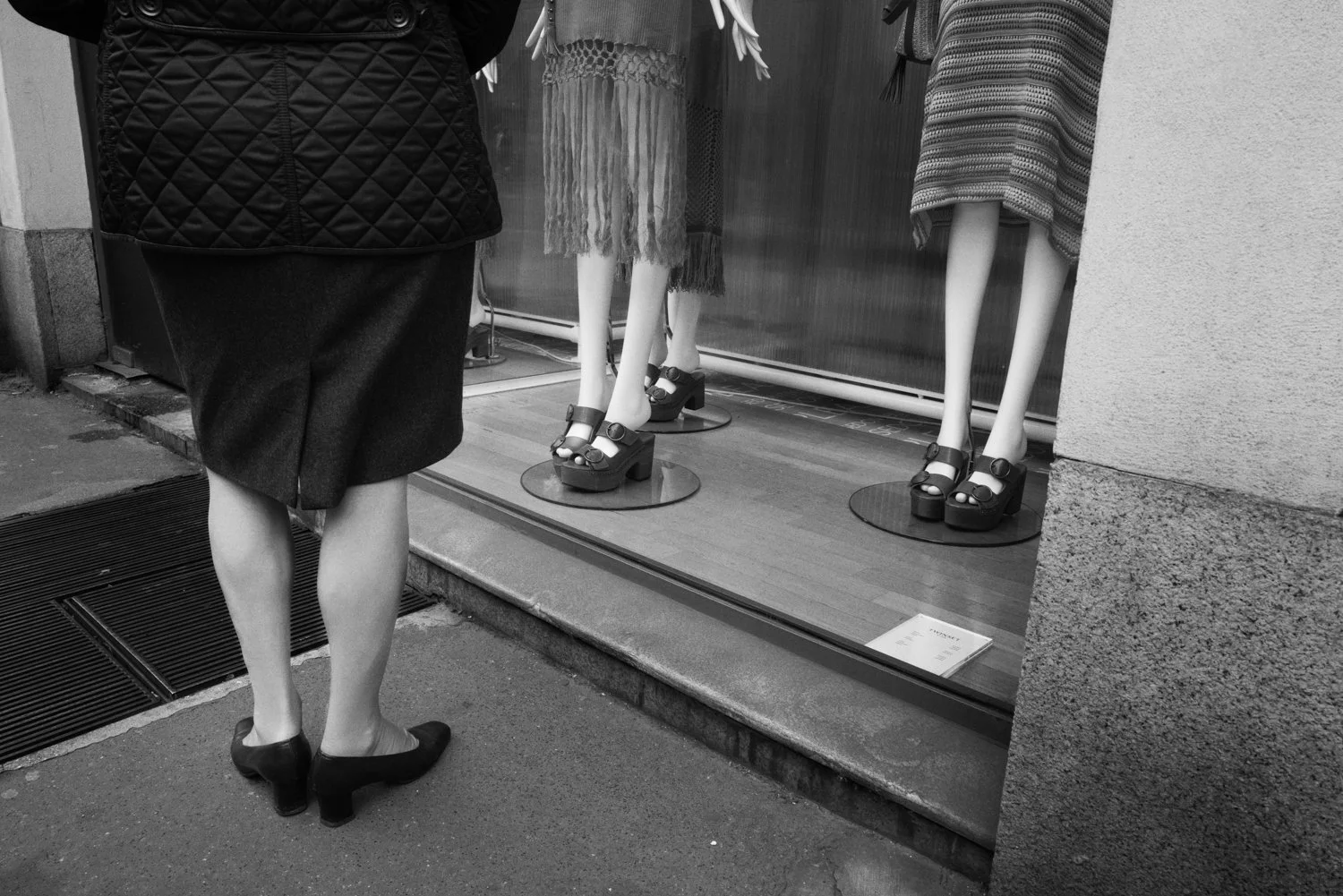 A woman stands in front of mannequins in a shop window