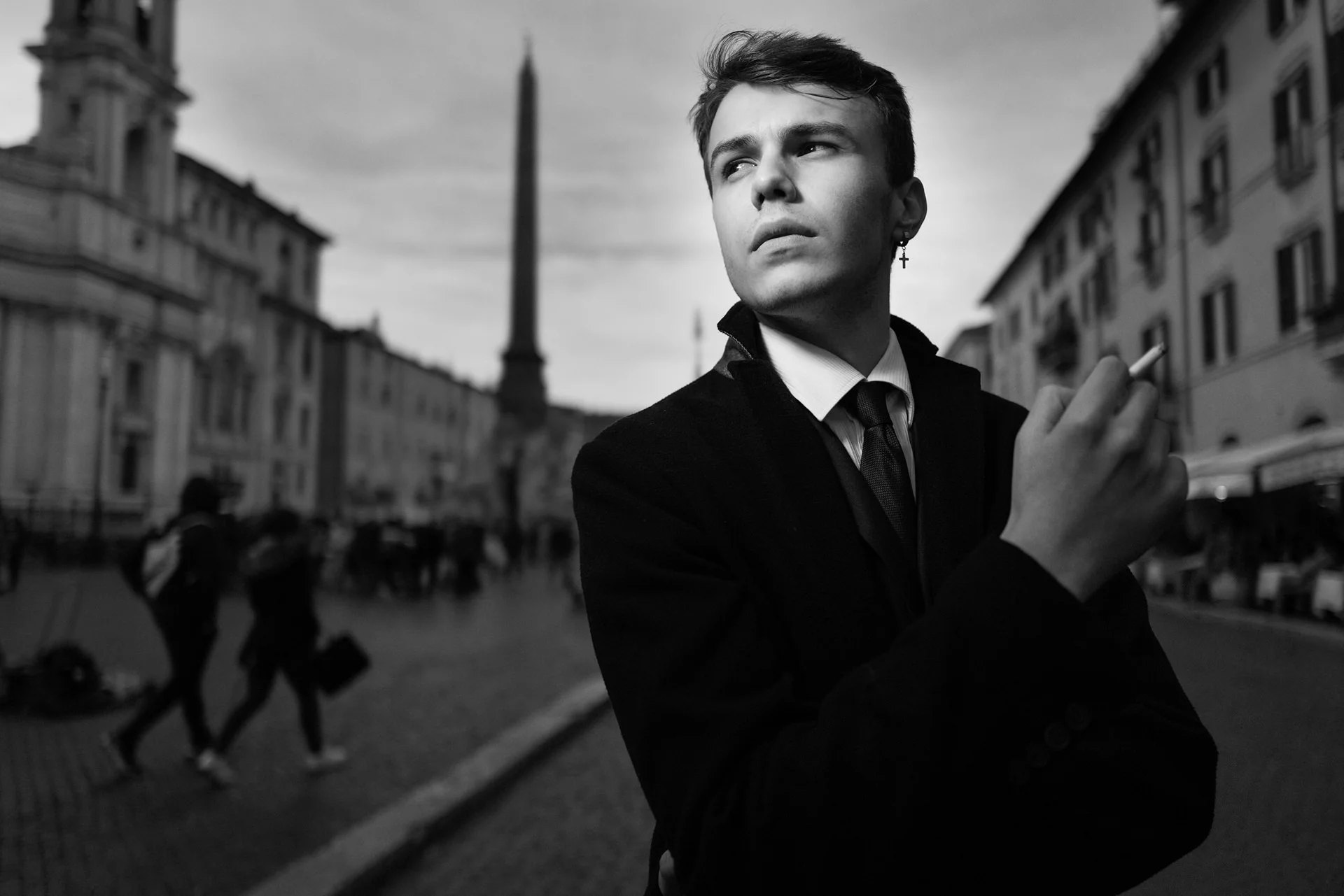 A young man in a dark coat looks aside in a square
