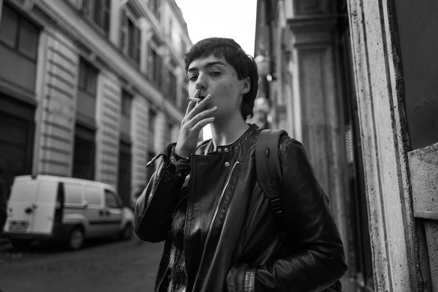 A young man smokes outside a stone building