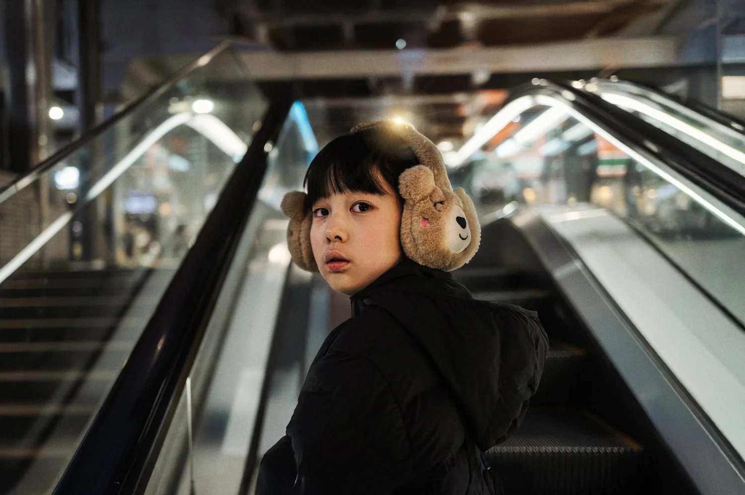A young person wearing headphones looks back on an escalator